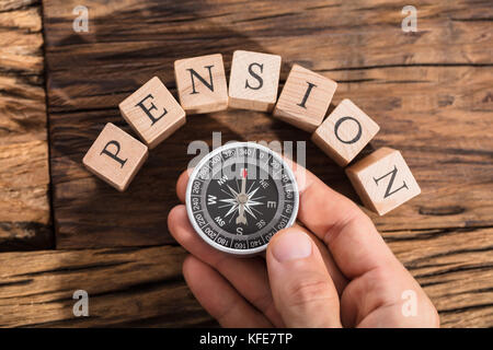 Close-up Of A Hand Holding Magnetic Compass In Front Of Pension Blocks Over The Desk Stock Photo