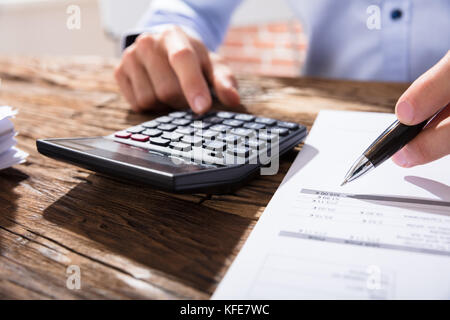 Close-up Of A Business Person Calculating Finance Using The Calculator Over The Wooden Desk Stock Photo
