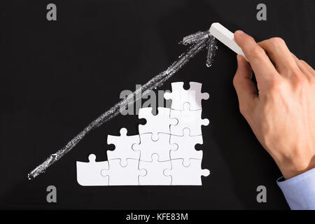 Close-up Of A Person Arranging White Puzzles Against Upward Arrow On Blackboard Stock Photo