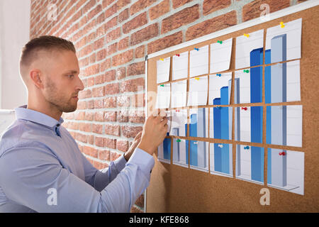 Close-up Of A Businessman Arranging Graph Made On Notes Over The Corkboard Stock Photo