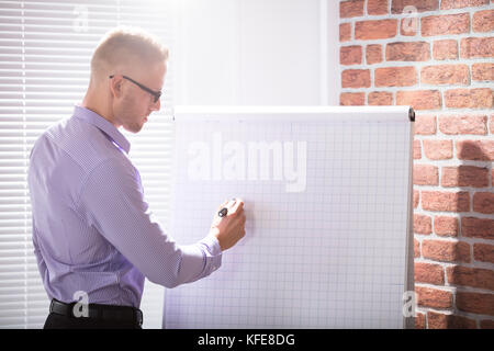 Close-up Of A Businessman Writing On Grid Flip Chart With Marker In Office Stock Photo