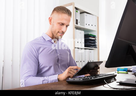 Smiling Businessman Using Digital Table In Front Of Computer At Workplace Stock Photo