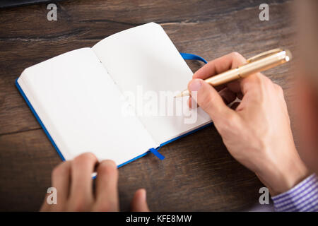 Elevated View Of A Businessperson Writing On Personal Diary Over The Wooden Desk Stock Photo