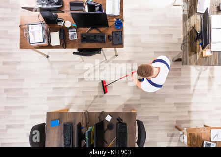 Elevated View Of Male Janitor Cleaning Floor With Broom At Workplace Stock Photo