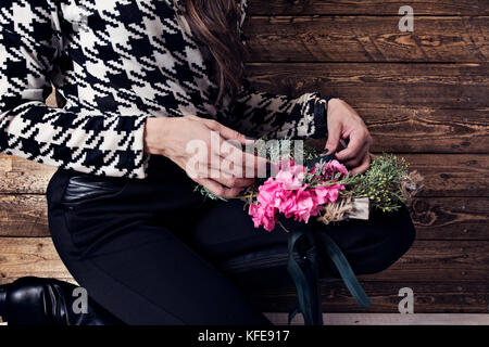 Woman wrapping Christmas wreath with natural flowers, rustic wooden wall background Stock Photo