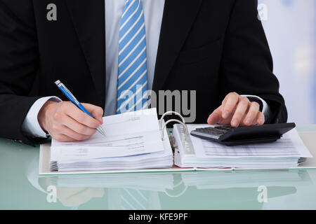 Midsection of young businessman calculating invoice at office desk Stock Photo