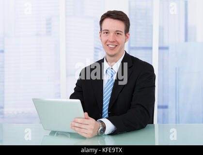 Portrait of confident young businessman using digital tablet at office desk Stock Photo