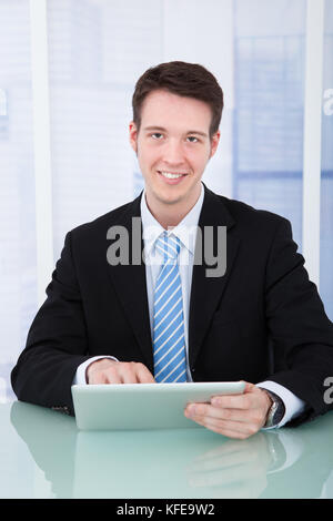 Portrait of confident young businessman using digital tablet at office desk Stock Photo