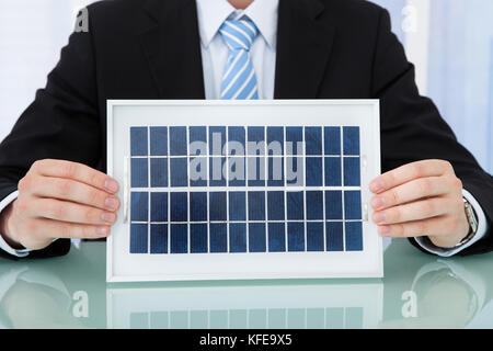 Midsection of businessman holding solar panel at office desk Stock Photo