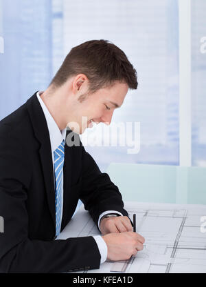 Side view of male architect working on blueprint at desk in office Stock Photo