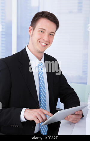 Portrait of confident young businessman using tablet computer at office desk Stock Photo
