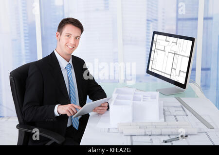 Portrait of confident young male architect using digital tablet at computer desk in office Stock Photo