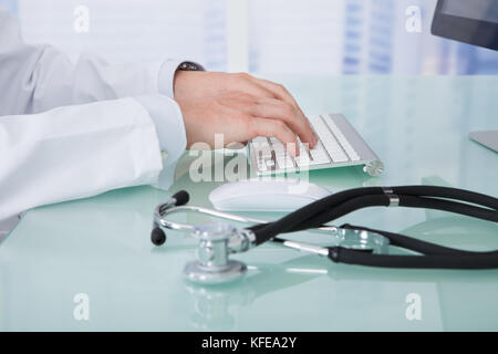 Midsection of young male doctor using computer at desk in clinic Stock Photo