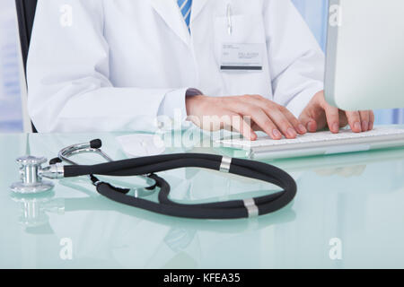 Midsection of young male doctor using computer at desk in clinic Stock Photo