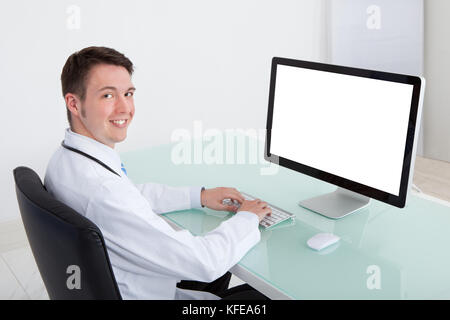 Portrait of confident young male doctor working on computer at desk in hospital Stock Photo