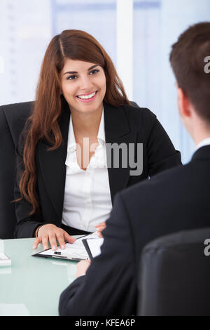 Happy young businesswoman interviewing male candidate at desk in office Stock Photo