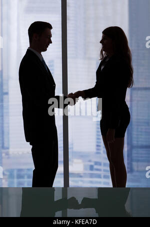 Side view of young businessman and businesswoman shaking hands in office Stock Photo