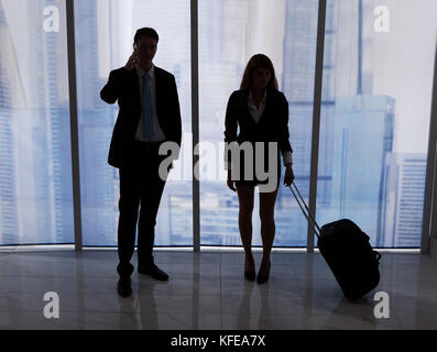 Full length of young businessman on call standing by female colleague with luggage in office Stock Photo