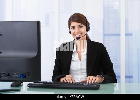 Portrait of confident young businesswoman wearing headset at computer desk Stock Photo