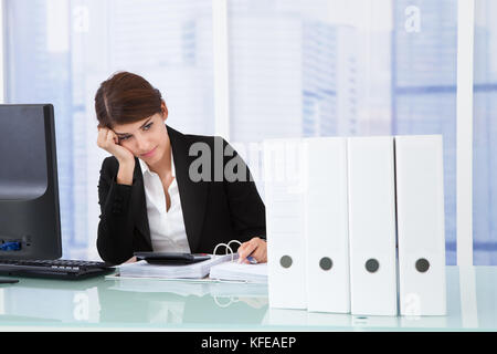 Worried businesswoman looking at binders on office desk Stock Photo