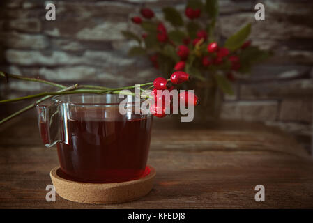 Cup of Tea from rosehip tea and bouquet of rose hips on the wooden background.Seasonal, vitamin drink.Cup Of Tea Or Coffee. Dried Fruits.Autumn and he Stock Photo