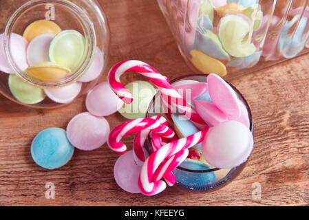 Colorful candies in jars on table on wooden background.Colorful candies spilling from a storage jar, over old wood background. Stock Photo