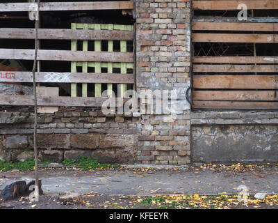 Old ruined city fence, columns of orange bricks and boards of boards. Stock Photo