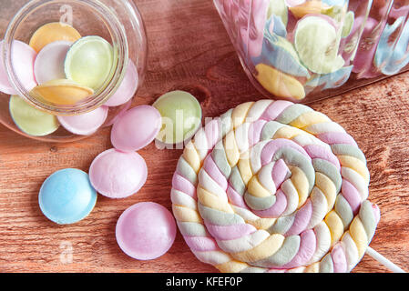 Colorful candies in jars on table on wooden background.Colorful candies spilling from a storage jar, over old wood background. Stock Photo