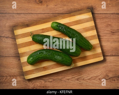 Pile of green cucumbers on wooden cutting board - closeup Stock Photo