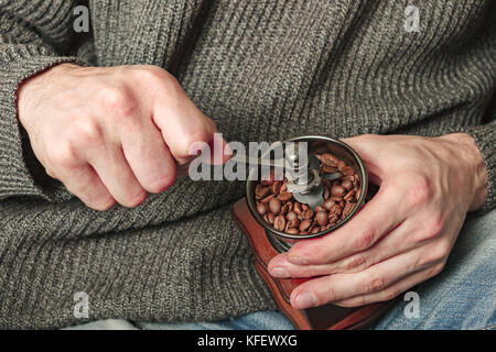 Men's hands with a coffee grinder against the gray woolen sweater in warm colors. Stock Photo