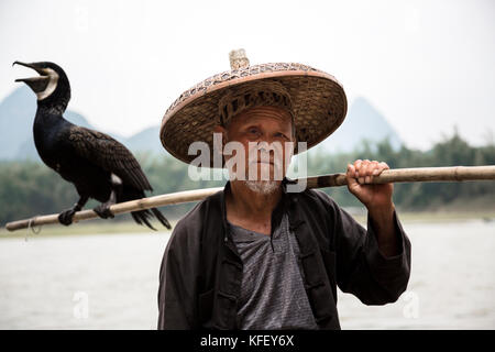 An old fisherman prepares for fishing in a traditional way using hand cormorant in the background of mountains in the province of Guangxi Stock Photo