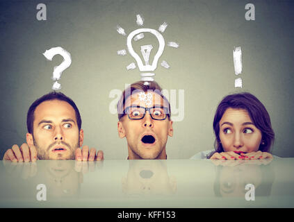 Scared anxious young people two men and a woman hiding peeking form under the table having questions and ideas to solve problem Stock Photo