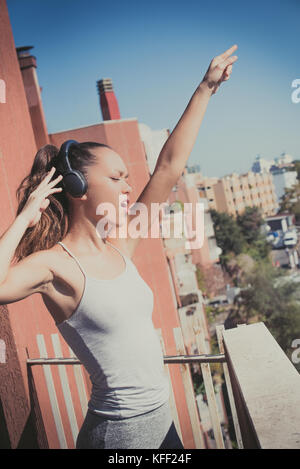 Young asian teen woman outdoor portrait closed eyes sunlight smiling dancing with headphones urban background city lifestyle Stock Photo