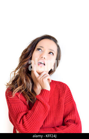 Young pretty asian teen woman in red dress looking up, finger over open mouth with deciding make a choice expression isolated on white background vert Stock Photo