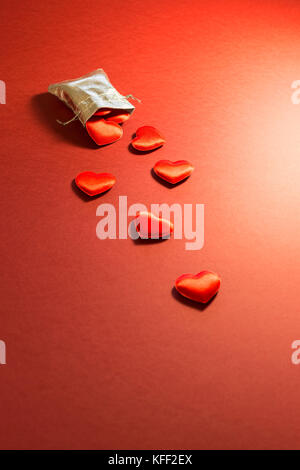 Close-up of a small shiny silver bag filled with cute red velvet hearts on red background. Concept of a romantic love gift for couples, valentines day Stock Photo