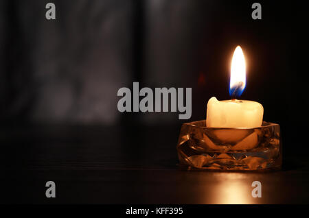 One lighting candle in glass candlestick against dark background Stock Photo