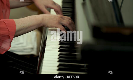 Girl's hands on the keyboard of the piano. The girl plays piano,close up piano. Hands on the white keys of the Piano Playing a Melody. Women's Hands on the keyboard, Playing the Notes Melody. Stock Photo