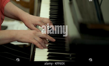 Girl's hands on the keyboard of the piano. The girl plays piano,close up piano. Hands on the white keys of the Piano Playing a Melody. Women's Hands on the keyboard, Playing the Notes Melody. Stock Photo