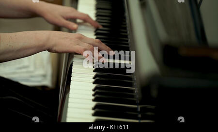 Girl's hands on the keyboard of the piano. The girl plays piano,close up piano. Hands on the white keys of the Piano Playing a Melody. Women's Hands on the keyboard, Playing the Notes Melody. Stock Photo