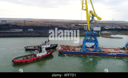 Towing cranes for containers. Large container ship pulled by tugboats. Top down aerial view. Container Cargo freight ship with working crane bridge in shipyard at dusk for Logistic Import Export background Stock Photo