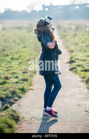 teenage girl dressed in denim in sunshine wearing virtual reality headset outdoors Stock Photo