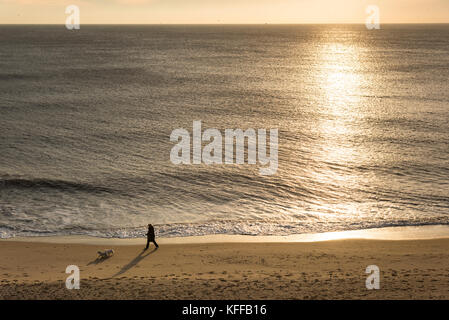 Southwold UK 28th October 2017. A woman walks her dog on the beach on a  cloudy and fresh morning on the East Anglian coast at sunrise over the North Sea. A chilly north west breeze has brought autumn temperatures down to around 9 degrees. Credit Julian Eales/Alamy Live News Stock Photo