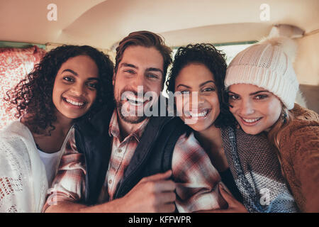 Friends on roadtrip taking selfie. Group of smiling man and women taking selfie in the van. Stock Photo