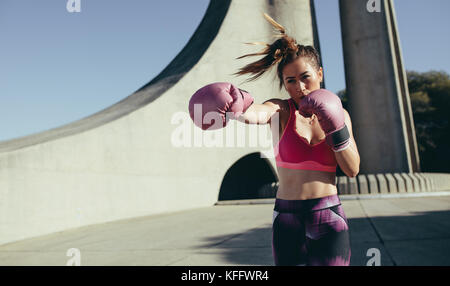 sportswoman doing boxing working outdoors. Female practicing boxing, throwing a punch in front. Stock Photo