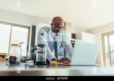 businessman using a laptop on kitchen table at home. Man working while having breakfast. Stock Photo