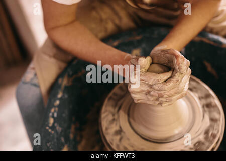 Potter making a clay pot on pottery wheel in workshop. Craftswoman moulding clay with hands on pottery wheel. Stock Photo