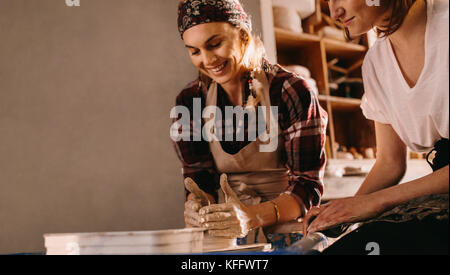 Woman potter teaching the art of pot making. Two women at a pottery workshop making clay pots. Stock Photo