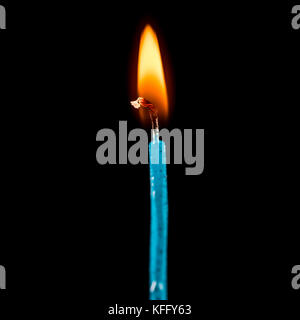 A macro shot of a single blue candle, burning against a black background. Stock Photo