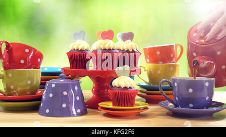 Colorful Mad Hatter style tea party with cupcakes and rainbow colored polka dot cups and saucers, with bokeh garden background and lens flare, pouring Stock Photo