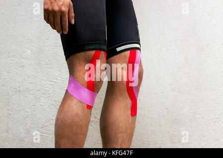 Horizontal photo of a male cyclist with kinesio tape on his knees standing in front of a white background Stock Photo